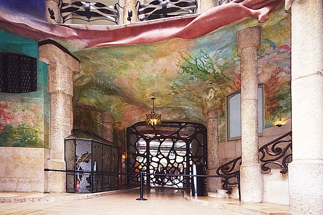 The entrance hall of Casa Milà, with its iron gate, stone columns and a ceiling painted with plants and flowers