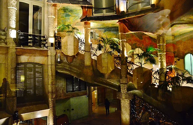 The stairway of La Pedrera winding through the inner courtyard, with palms, iron railings and painted walls